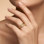 Close-up of a hand wearing two gold rings on a beige background