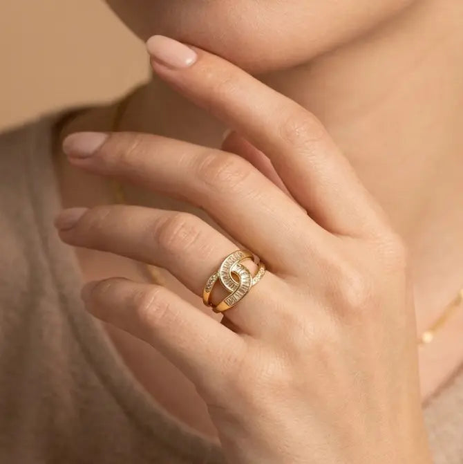 Close-up of a hand wearing a gold ring with a diamond, against a neutral background.