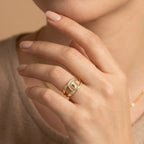 Close-up of a hand wearing a gold ring with a diamond, against a neutral background.