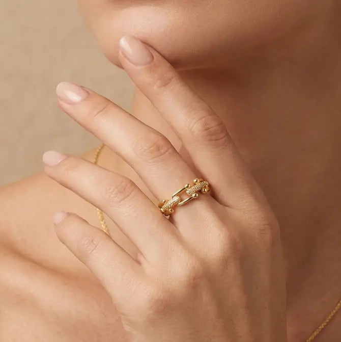 Close-up of a hand wearing a gold ring with a pearl on a beige background