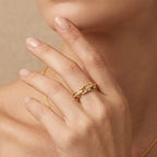 Close-up of a hand wearing a gold ring with a pearl on a beige background