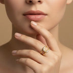 Close-up of a hand wearing a gold ring with a diamond on a beige background