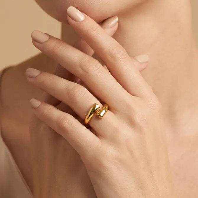 Close-up of a hand wearing a gold ring on a beige background