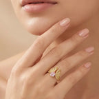 Close-up of a hand wearing a gold ring with a pink gemstone on a beige background