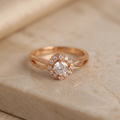 Rose gold ring with a diamond on a beige stone surface