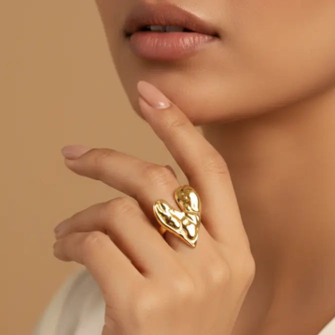 Close-up of a hand wearing a gold heart-shaped ring against a beige background