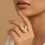 Close-up of a hand wearing a gold heart-shaped ring against a beige background